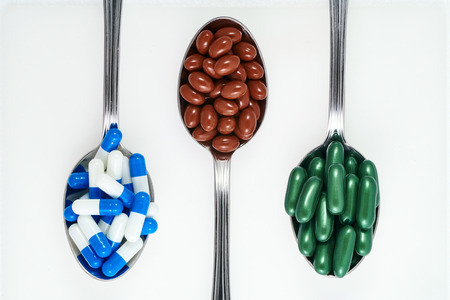 Supplement and medecine pills on three spoons on white backgroundの写真素材