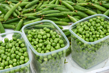 Transparent plastic containers filled with freshly peeled fresh green peas for sale at the market. On the background other unpeeled peas, out of focus.の写真素材