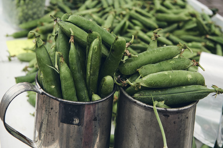 Two metal mugs full of peas. In the background other blurry peas. Matte style