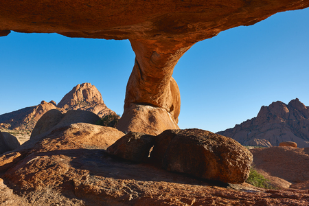 Under the rock arch in Damaraland in Namibia, in the background the famous Spitzkoppe, the Matterhorn of Africa.の写真素材