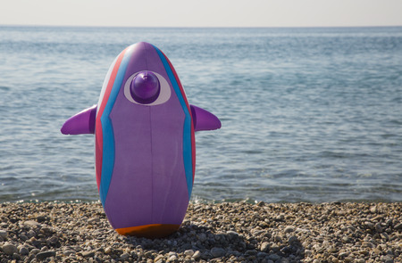 A penguin toy balloon on the beach looking at the seaの写真素材