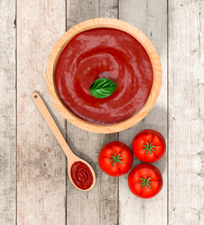 red tomatoes with a spoon and a bowl with tomato sauce, on wooden background (3d render)の写真素材