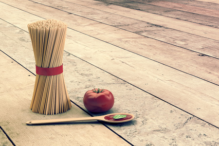 bunch of spaghetti with a tomato and a ladle with tomato sauce, on wooden background, empty space at the right (3d render)の写真素材