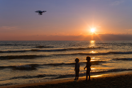 two children looking at a drone in flight on the beach at sunsetの写真素材