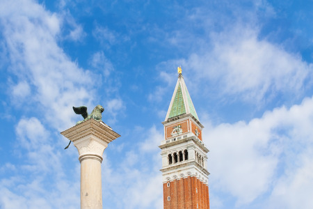 St. mark39s square column with lion39s famous bronze statues symbol of venice and bell tower in a sunny day blue sky some cloudsの写真素材