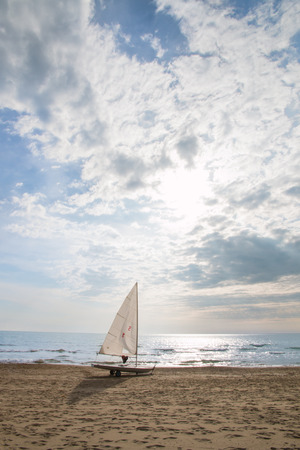 small sailboat on a cart at the beach ready to sailing. life jacket hanging from the boom. sun is shining in a cloudy skyの写真素材