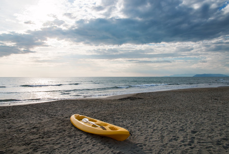 yellow plastic canoe two seater with on a sandy beach near to the sea sunlight filters through cloudsの写真素材