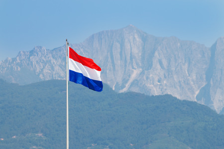 flag of the Netherlands waves in the wind on a tall pole in Forte dei Marmi. Monte Altissimo of Allpi Apuane blurred in backgroundの写真素材