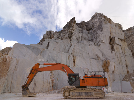 Orange cingulate Excavator in a white marble Carrara's quarry in Apuan Alps