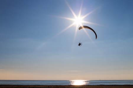 Motor Paraglider flying near the sun over  the sea and the beach