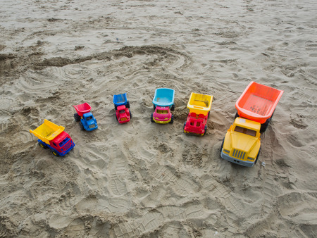 Group of toy working trucks of different sizes and colors arranged in a semicircle on a sandy beach. copy spaceの写真素材