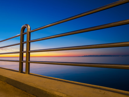 perspective view railing made of stainless steel to prevent corrosion and oxidation next to the sea. Colorful sunset , sea and coastline in backgroundの写真素材