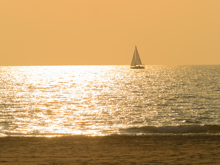 silhouette of a sailing boat surrounded by sun glitters  sea on a beautiful sunset with calm golden seaの写真素材