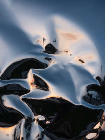 Curvy surface of mirror polished shiny metal reflecting lights and shadows and the colors of the sky at eveningの写真素材