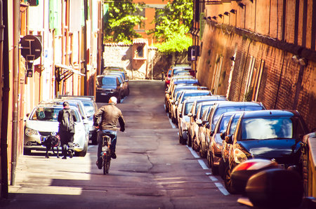 Bologna, Italy, April 25 2016: bald man cross street with bicycle alongside a row of parked carsのeditorial素材