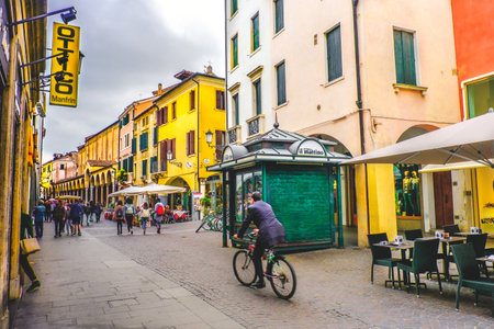 daily life in Italy. A business man in bicycle crossing one of the central roads of Padua passing by a green newsstand kiosk on the street (Padova, Italy, 24 Apr 2017)のeditorial素材