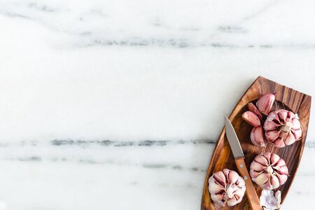 Garlic with knife on a white marble surface.