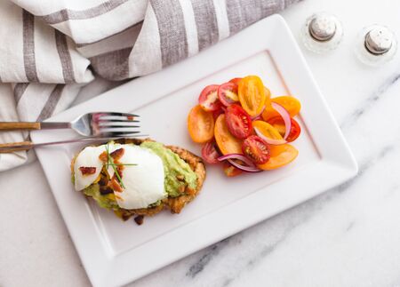 Avocado toast with poached egg and tomato salad  on a a marble top for brunch.の写真素材