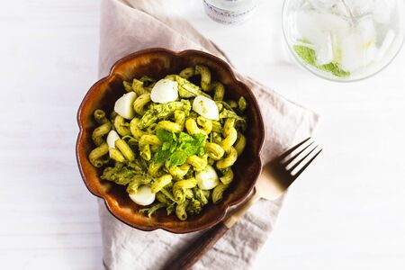 Homemade pasta salad with pesto and buffalo mozzarella on a white surface and rustic napkin.の写真素材