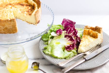Quiche with colorful salad and dressing on a marble surface.