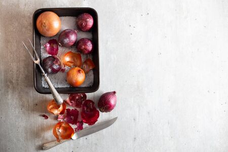 Onions in a baking sheet with salt and on a gray surface.の写真素材