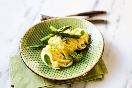 Pasta with asparagus and basil on a green ceramic and white surface.の写真素材