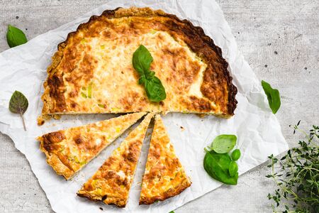 Leek and bacon quiche on a gray surface with fresh basil leaves