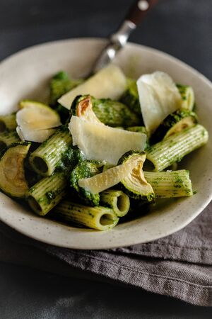 Green pasta with zucchini and parmesan cheese on a gray surface.の写真素材