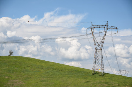 power lines on a green hill with lone tree under cloudy blue sky
