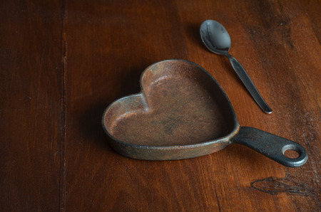 hearth shaped cast iron  saucepan with silver tea spoon on wood tableの写真素材