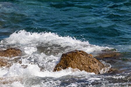 Ligurian sea waves crashing on the rocks on a sunny dayの写真素材