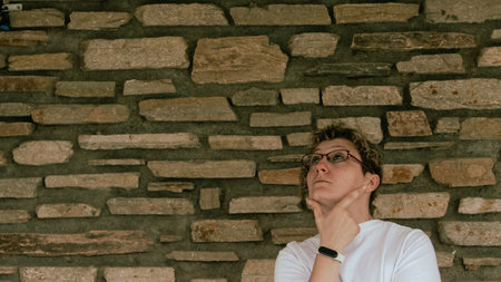 close up of caucasian girl in glasses and tshirt thoughtfully with hand to her face and looking up, rustic backgroundの写真素材