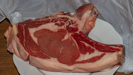 A premium cut of raw beef steak, rich in marbling and color, presented on a white plate, ready for culinary preparationの写真素材