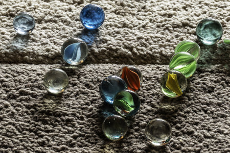 diverse assortment of colorful glass marbles scattered across a textured gray rug, each marble reflecting light differently, adding a playful and vibrant element to the rough fabric backgroundの写真素材