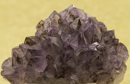 Exquisite amethyst crystal cluster showcased against a yellow backdrop, capturing the gem's rich purple hues and natural geometric facetsの写真素材