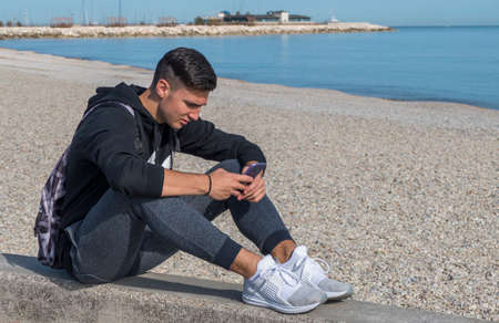 The end of the summer with a boy that play with a smartphone in a beachの写真素材