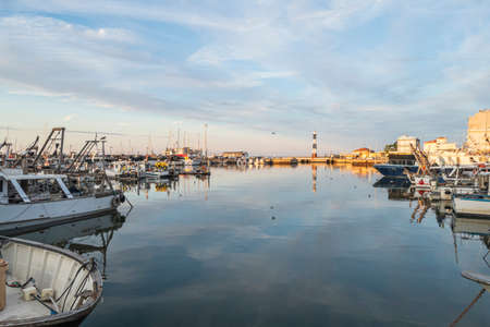 Cattolica, Italy - 04-08-2021: The port of Cattolica with the boats and the lighthouse reflecting in the water at sunsetのeditorial素材
