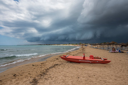 Portopalo, Italy - 09-17-2022: Beautiful beach in Sicily with a red patino in the foreground and a sky with black and stormy cloudsのeditorial素材
