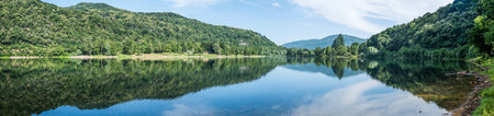 Panoramic view of mountains, trees and clouds perfectly reflected in a blue lakeの写真素材