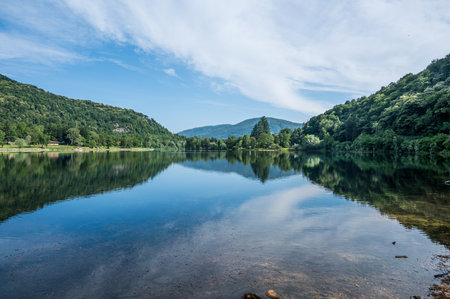 Panoramic view of mountains, trees and clouds perfectly reflected in a blue lakeの写真素材