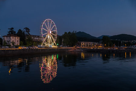 Luino, Italy: 05-18-2021: Ferris wheel illuminated in the evening with the lights reflecting on the Lake Maggiore in Luinoのeditorial素材