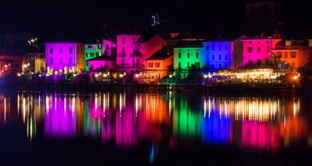 Porto Ceresio, Italy: 12-25-2021: Houses illuminated by searchlights on Christmas night, by colored lights reflecting on the water of the Lake of Luganoのeditorial素材