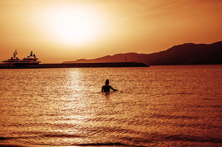 Beautiful sunset with red colors on the sea with a girl in the water turned towards the low sun on the horizonの写真素材