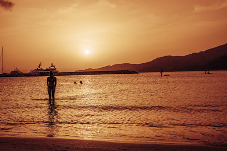 Beautiful sunset with red colors on the sea with a girl coming out of the waterの写真素材