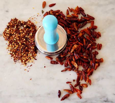 Dried red chili peppers and seeds around a steel meat tenderizer on a marble tableの写真素材