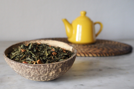 Dried green tea leaves in a coconut shell with a yellow teapot on a backgroundの写真素材