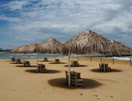 Straw umbrellas and beach furniture in a beautiful sandy beach under a blue sky with many cloudsの写真素材