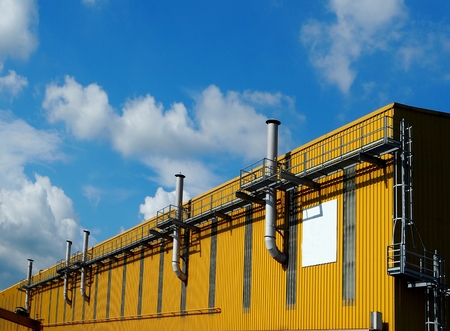 Chimneys on a yellow factory facade under blue sky with cloudsの写真素材