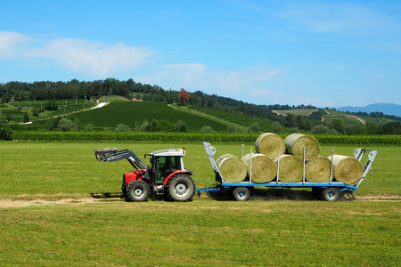 A tractor with its trailer loaded with hay bales on a background of the beautiful landscape.の写真素材