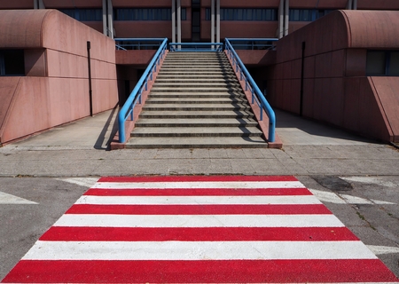 Urban background, red and white pedestrian crossing in front of a stone staircase of a modern buildingの写真素材